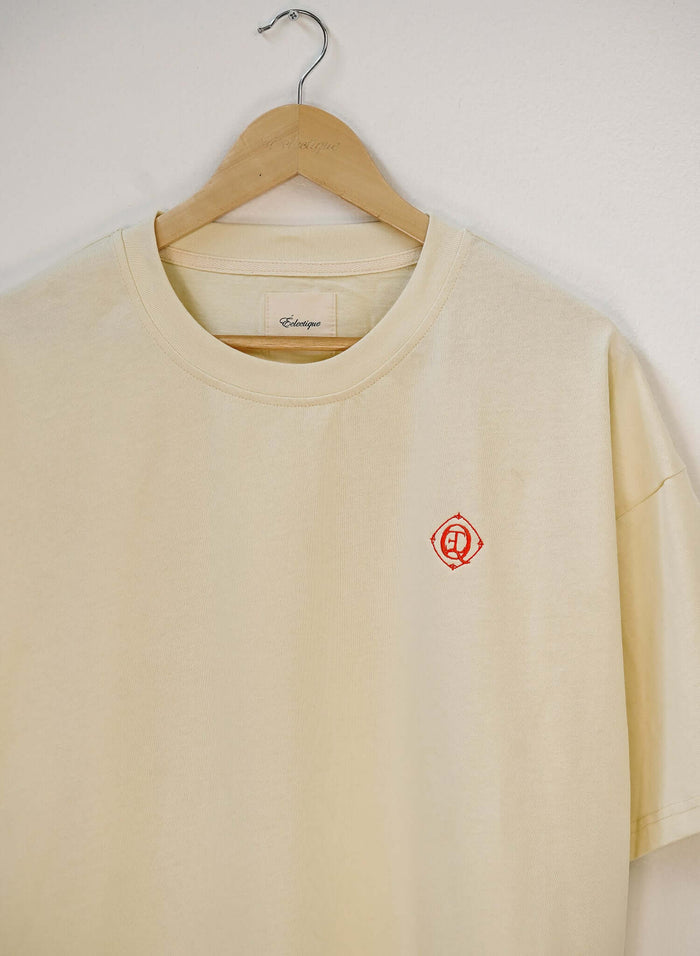 Monogram embroidered cotton t-shirt in French vanilla hanging on a wooden hanger, featuring an embroidered logo.