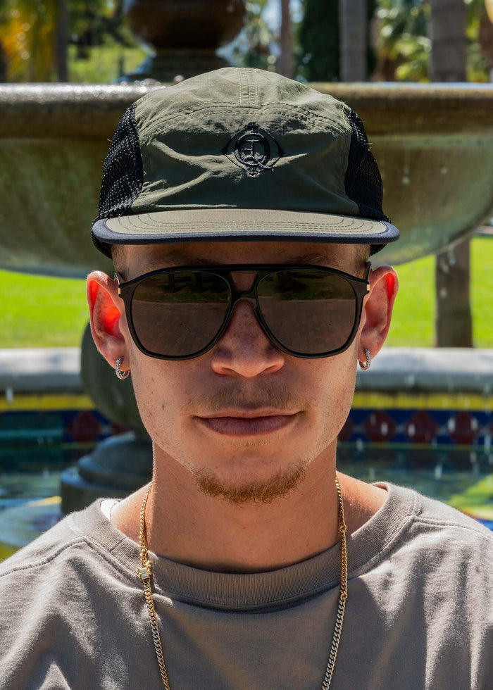 Monogram Performance Mesh Cap Olive worn by a person outdoors with sunglasses in a sunny setting.