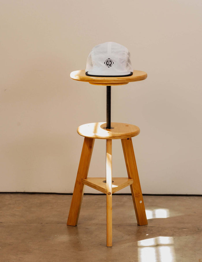 Monogram Performance Mesh Cap displayed on a wooden stool, highlighting its lightweight design and signature black logo.