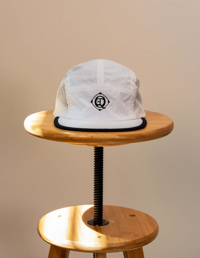 Monogram performance mesh cap in white displayed on a wooden stool, featuring breathable mesh side panels and signature logo.