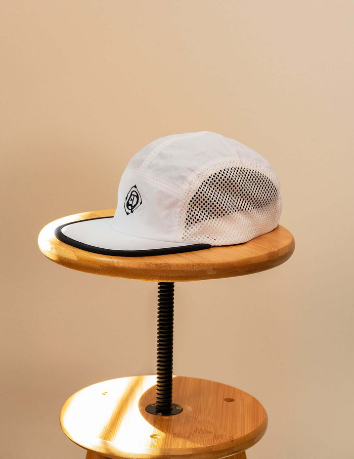 Monogram Performance Mesh Cap white displayed on a wooden stool, showcasing its mesh sides and logo design.
