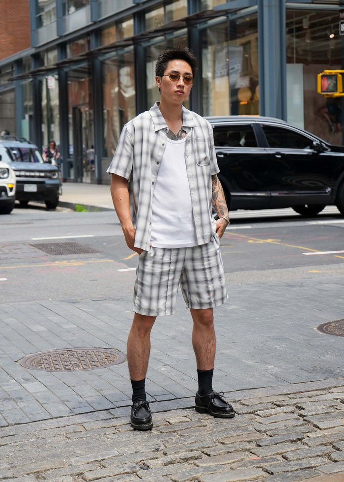 Monotone plaid button-up shirt styled in a relaxed fit, paired with matching shorts on city street.