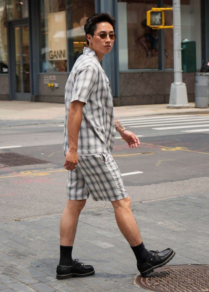 Man wearing a monotone plaid button-up shirt and shorts walking on the street, showcasing a modern casual look.