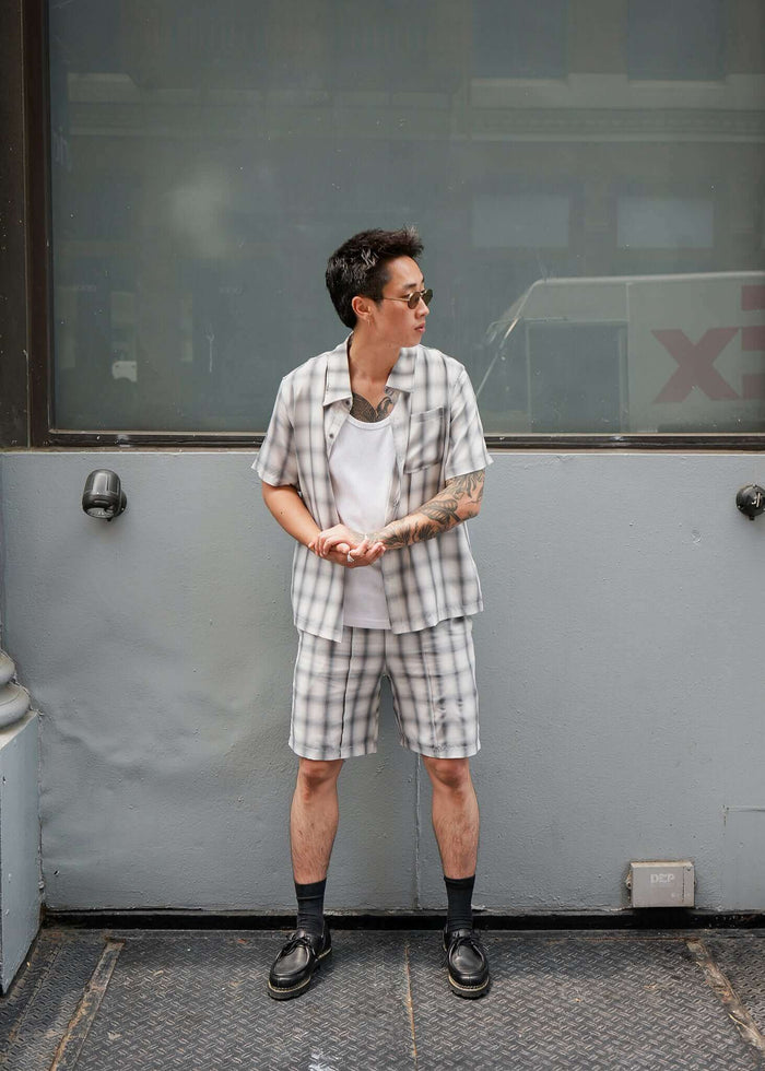 Person wearing a monotone plaid button-up shirt with matching shorts, styled casually in an urban setting.