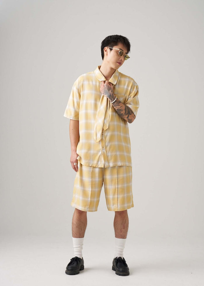Model wearing an ombre plaid shirt in yellow, paired with matching shorts for a trendy summer look.