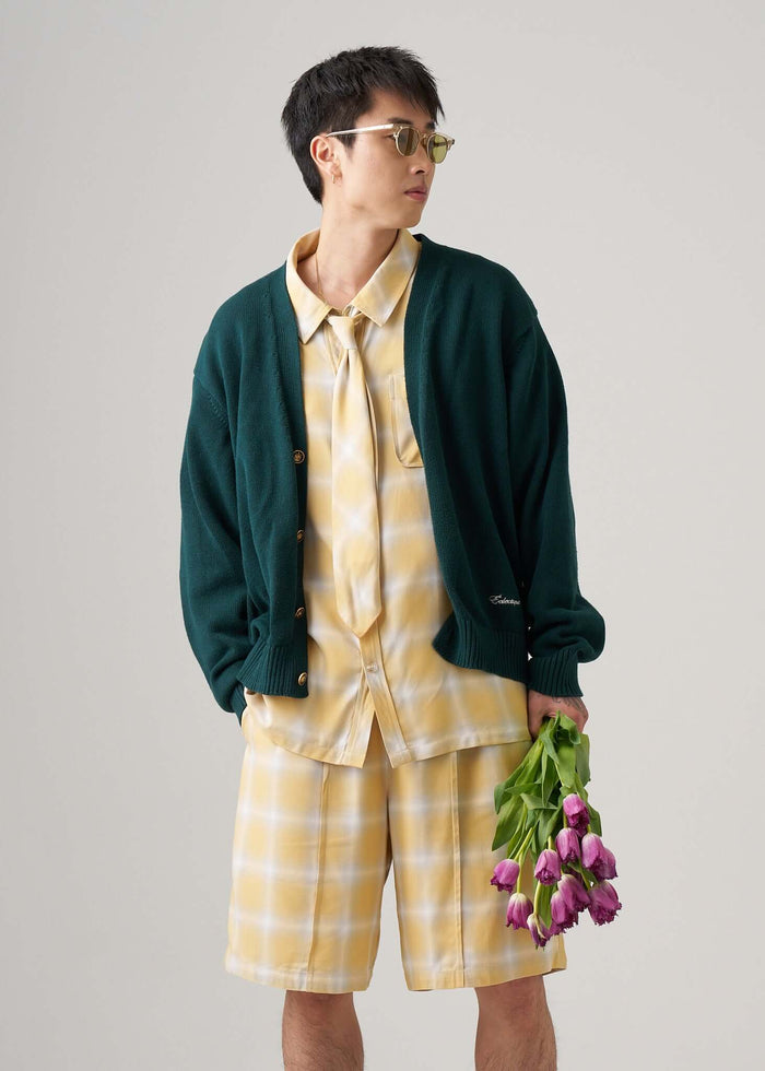 Man wearing ombre plaid shorts in yellow with a green cardigan, holding tulips, showcasing a stylish summer outfit.