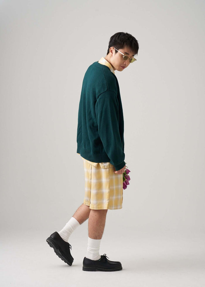 Ombre plaid shorts in yellow worn by a model with a green sweater and sunglasses, styled for summer looks.