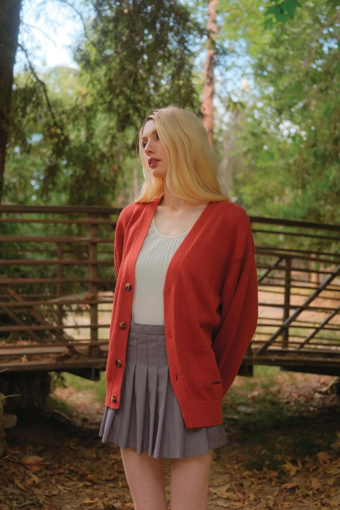 Female model in orange v neck cardigan in Sunburst near wooden bridge