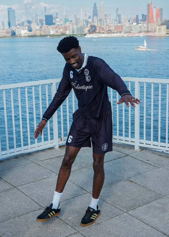 Model showcasing performance soccer shorts by Éclectique near waterfront with city skyline in background.