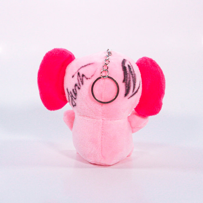 A small pink plush elephant keychain from Pink Elefants, with large pink ears, seen from the back and featuring black markings or signatures on its head.