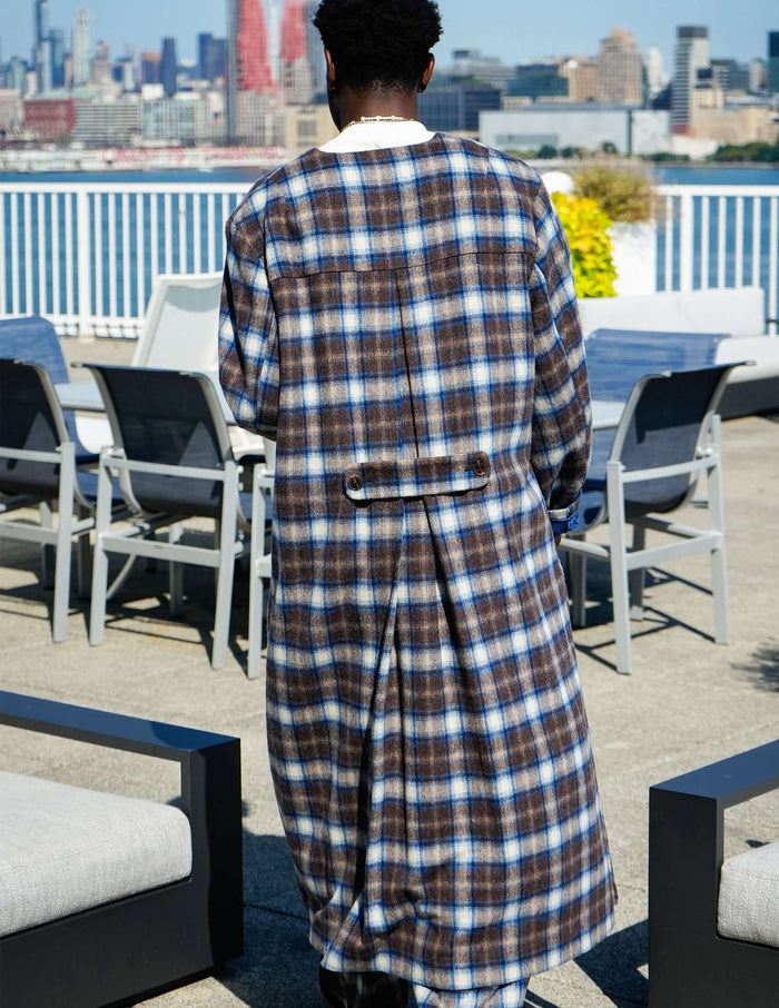 Back view of a man wearing a Kanso Plaid Collarless Long Coat, showcasing the elegant plaid pattern against a city backdrop.