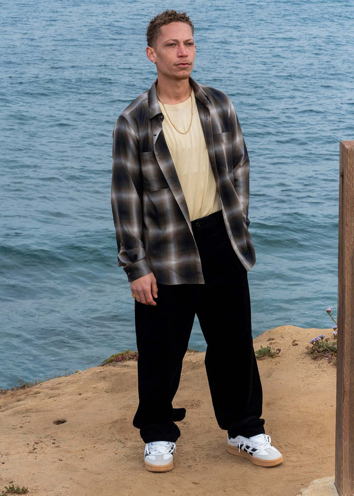 Man wearing a Plaid Cotton Button-up Shirt, styled with black pants and sneakers by the seaside.