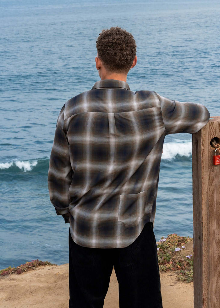 Man wearing a Plaid Cotton Button-up Shirt, standing by the ocean, showcasing classic style and modern design.