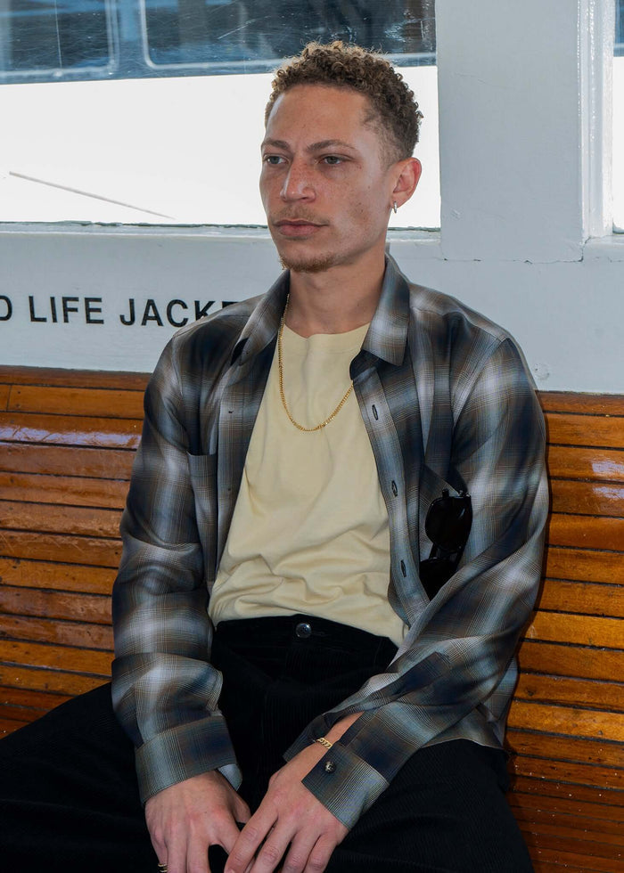 Man wearing a Plaid Cotton Button-Up Shirt with a yellow t-shirt, seated on a boat, showcasing a classic yet modern style.