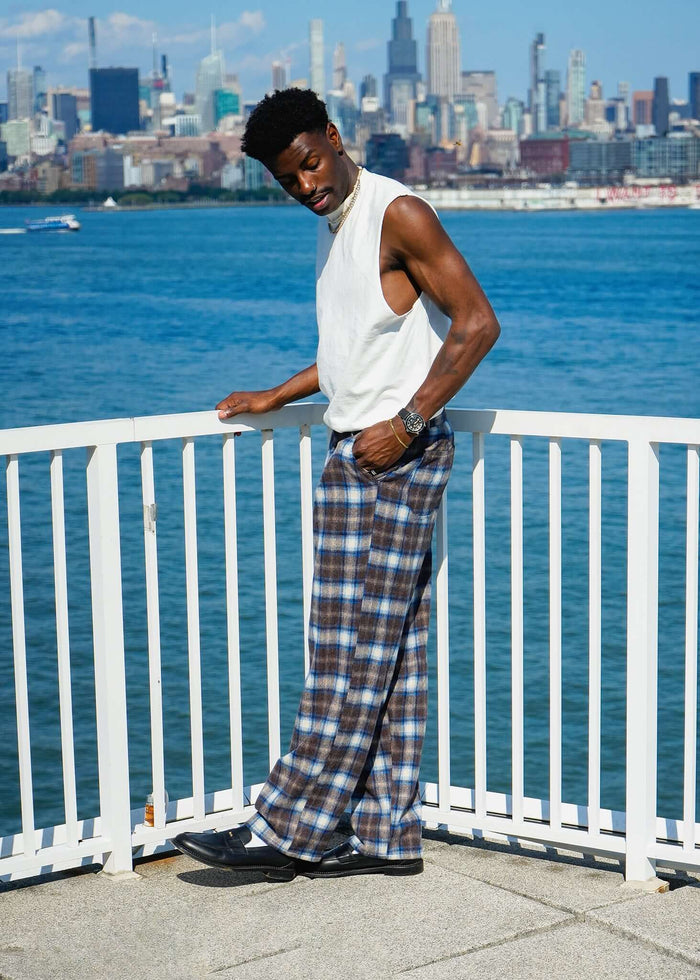 Man wearing Mercer Plaid Pleated Trousers near the waterfront with a city skyline backdrop.