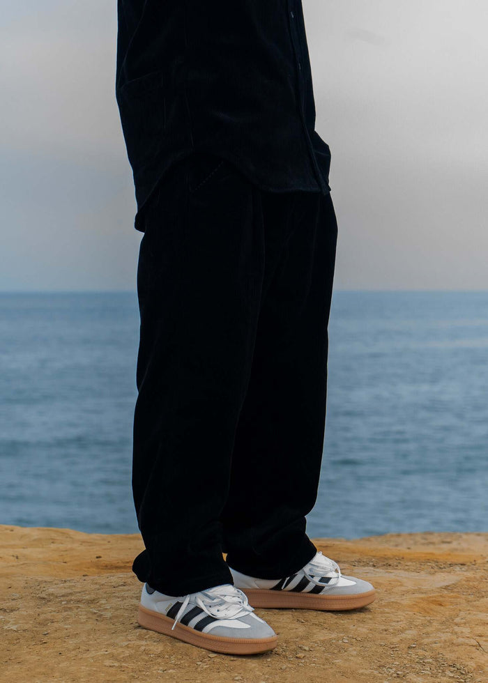 Model showcasing Pleated Corduroy Trousers by Mercer, standing near the ocean.