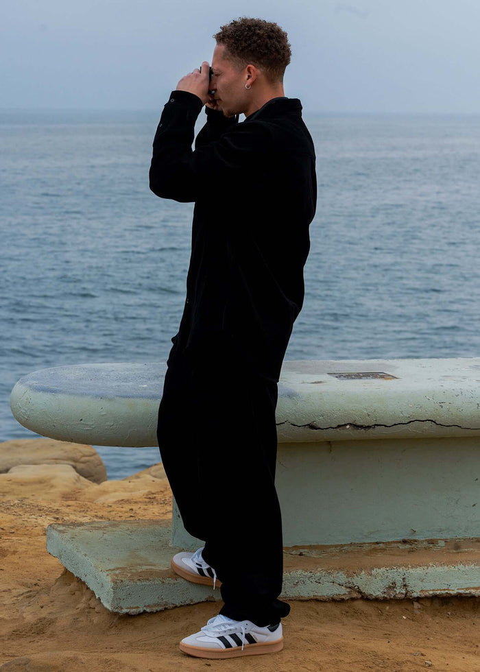Person wearing Pleated Corduroy Trousers by Mercer, standing by the water and capturing a photo.