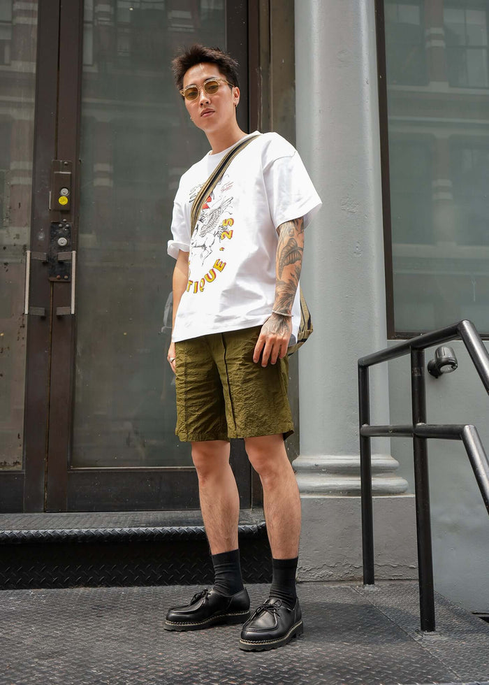 Stylish model wearing Racing Graphic T-shirt from Éclectique with shorts and shoes, showcasing a relaxed urban look.