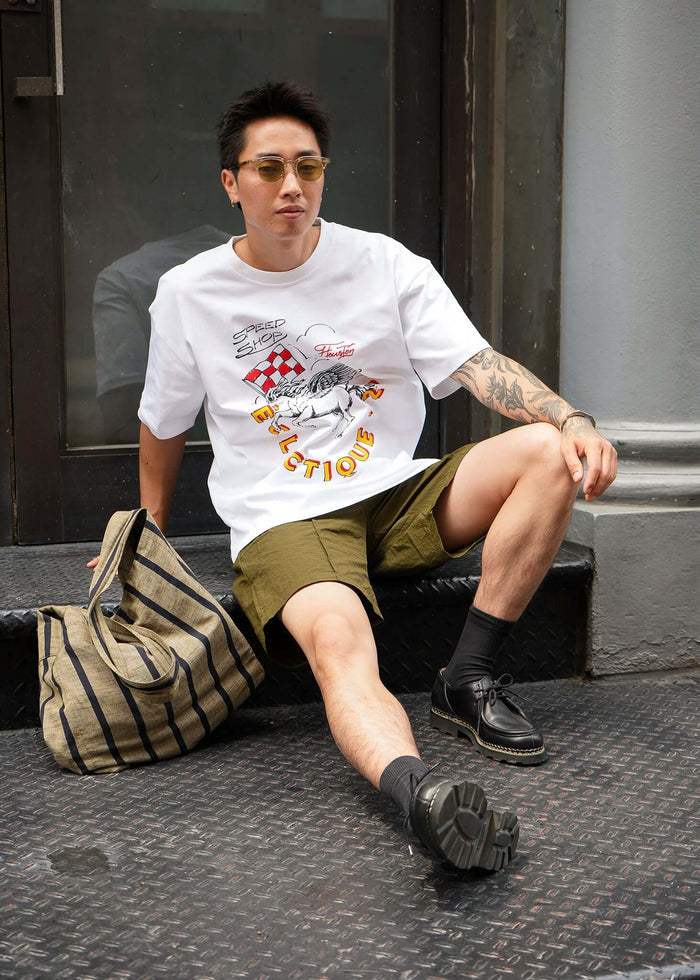 Man sitting with a Racing Graphic T-shirt from Éclectique Speed Shop, pairing it with shorts and sunglasses.