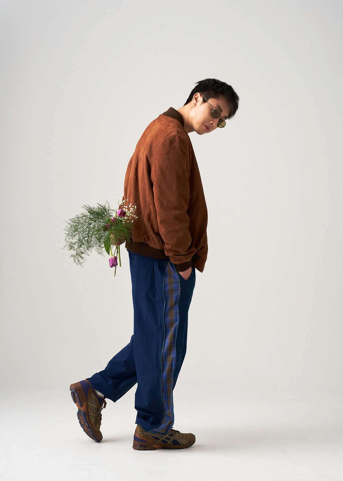 Model wearing Reversible Windbreaker Pants with a brown bomber jacket and flowers, showcasing a stylish casual look.