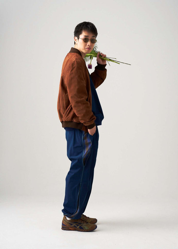 Model wearing Reversible Windbreaker Pants, showcasing a stylish look with sunglasses and a flower in hand.