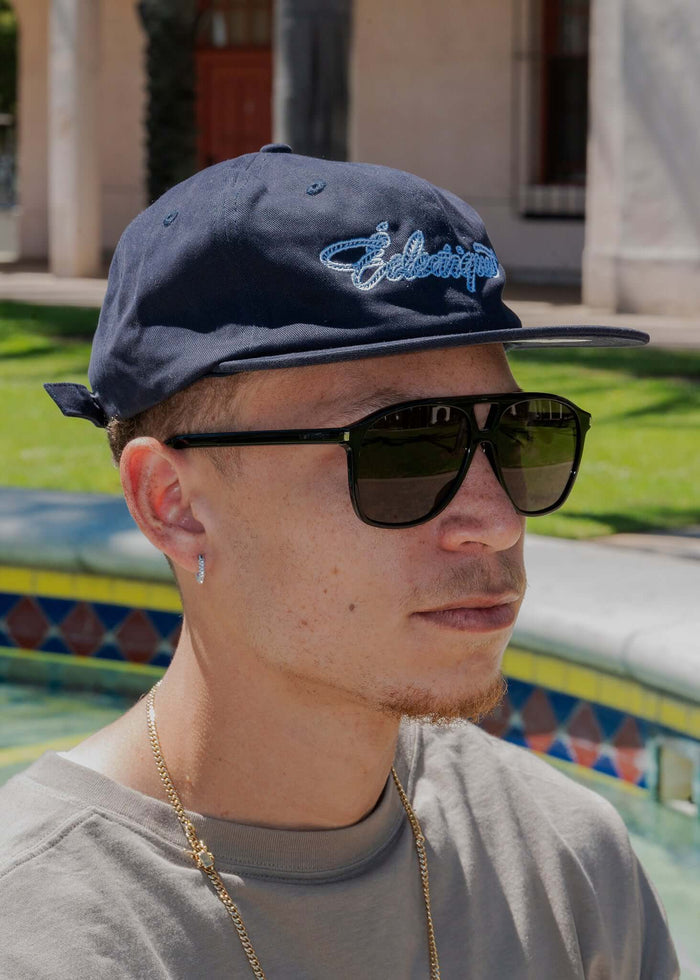 Model wearing Rope Script Dad Hat with sunglasses in a sunny outdoor setting, showcasing its embroidered design.