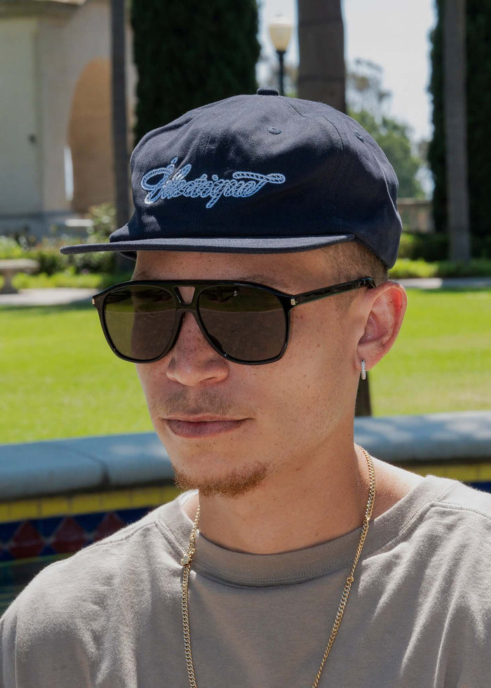 Man wearing a Rope Script Dad Hat outdoors, featuring embroidered design and sunglasses.