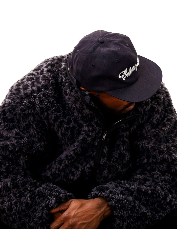 Person wearing a black Rope Script Dad Hat with embroidered script, seated in a cozy fleece jacket.