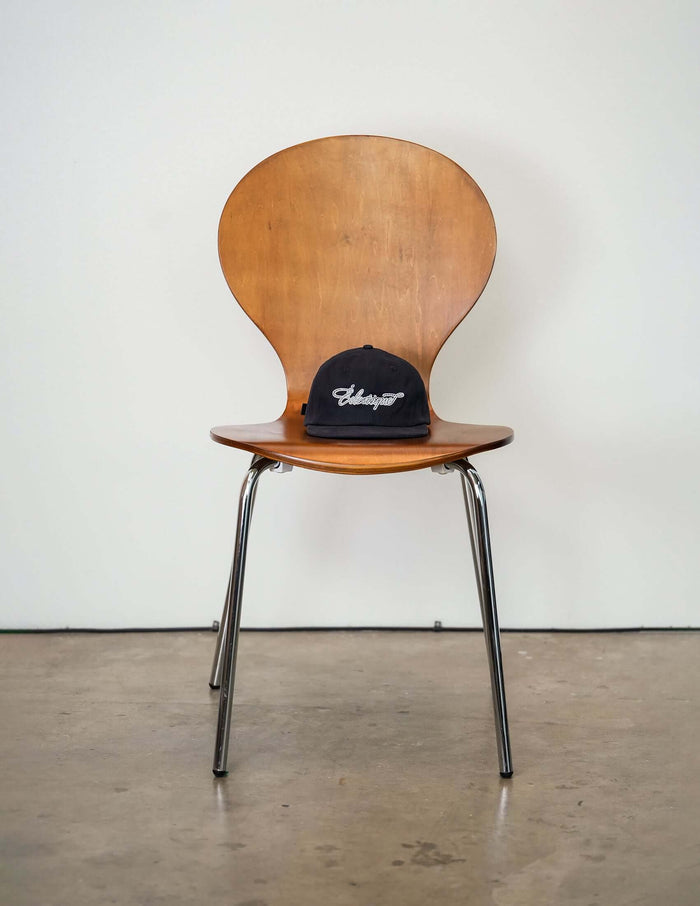 Rope script dad hat placed on a stylish wooden chair, showcasing its relaxed design and casual appeal.