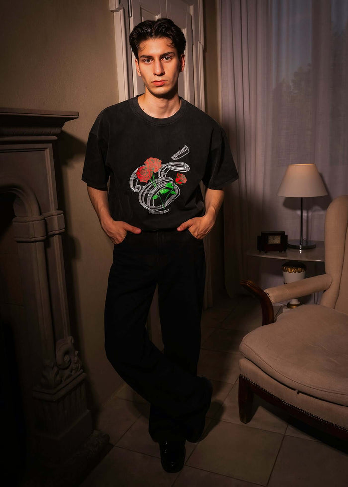 Model wearing Éclectique Rose Graphic T-Shirt with detailed roses, styled in a cozy indoor setting.