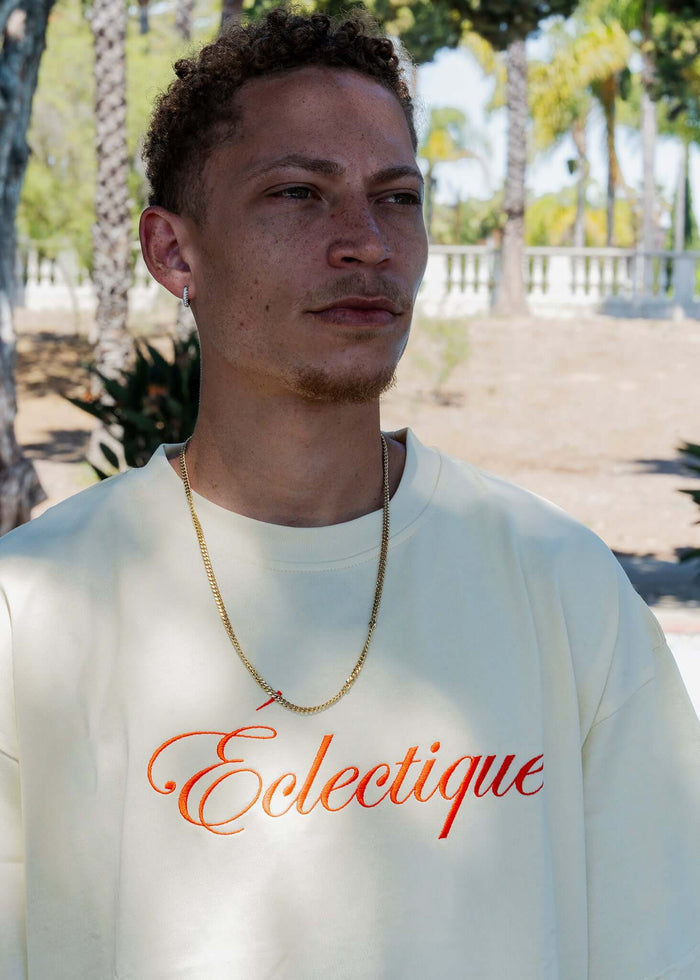 Model wearing script logo embroidered cotton t-shirt in French vanilla with the Éclectique logo.