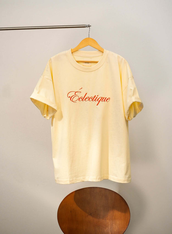 Script logo embroidered cotton t-shirt in French vanilla color hanging on display.