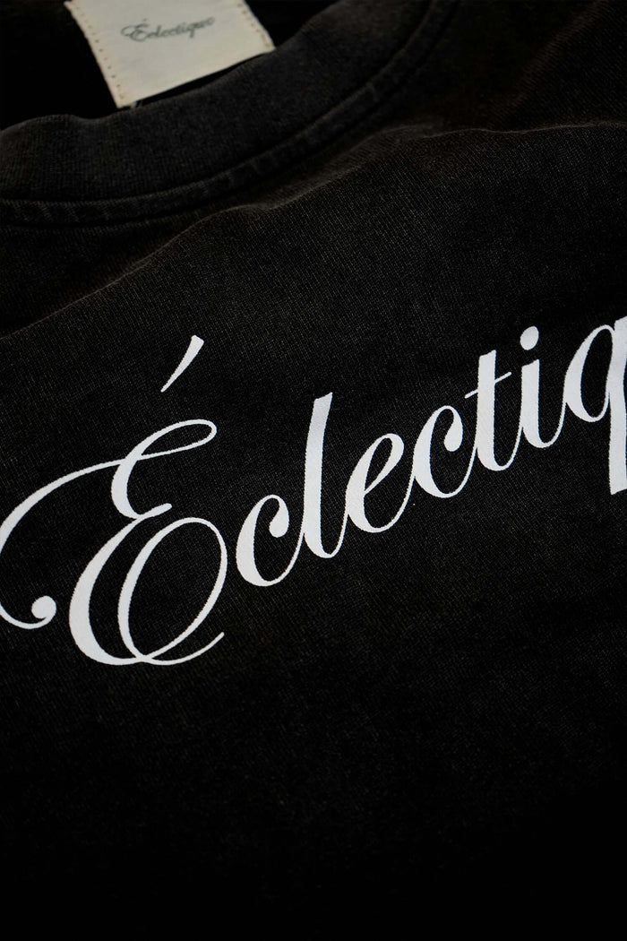 Close-up of the Éclectique script logo on an acid-wash black heavyweight script logo t-shirt.