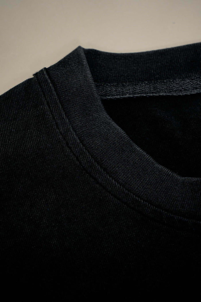 Close-up of the ribbed crewneck of a script logo T-shirt in acid-wash black heavyweight cotton.