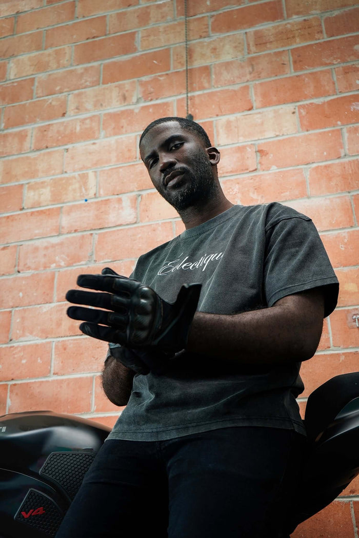 Model wearing a script logo t-shirt in acid-wash black, preparing to ride a motorcycle.