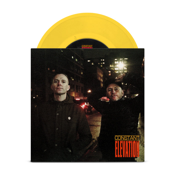 Two men stand on a city street at night with blurred lights behind them. The Constant Elevation album cover displays yellow and red text, with a partially visible yellow vinyl record above. Brand name: Constant Elevation.