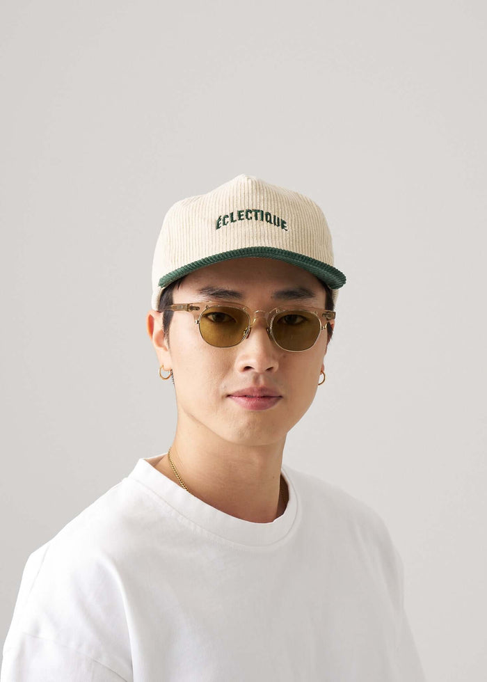 Two tone snapback hat in green and natural worn by a model with sunglasses and a white shirt.