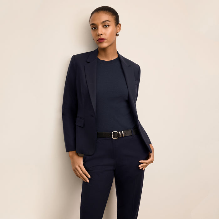 Woman wearing a navy suit with a belt against a beige background | Lead