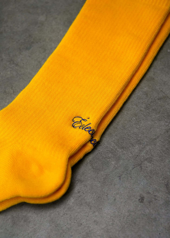 Spectra yellow crew socks from Éclectique laying flat, showcasing bright yellow color and brand logo.